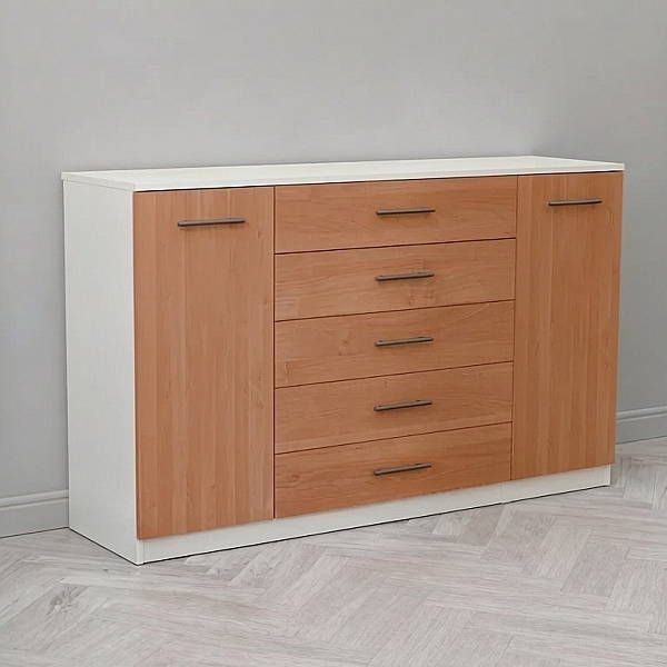 Широкий домашний комод ГрандМод-17 высотой 98 см от мебельной фабрики Мультимебель, сфотографированный сбоку под углом. Прочный каркас мебели окрашен в чистый белый цвет, а все выдвижные ящики и боковые распашные дверцы имеют приятный рыжевато-медовый оттенок натуральной ольхи. На светлых деревянных фасадах четко выделяются длинные горизонтальные металлические ручки-релинги. Мебель аккуратно установлена в светлой комнате у стены.